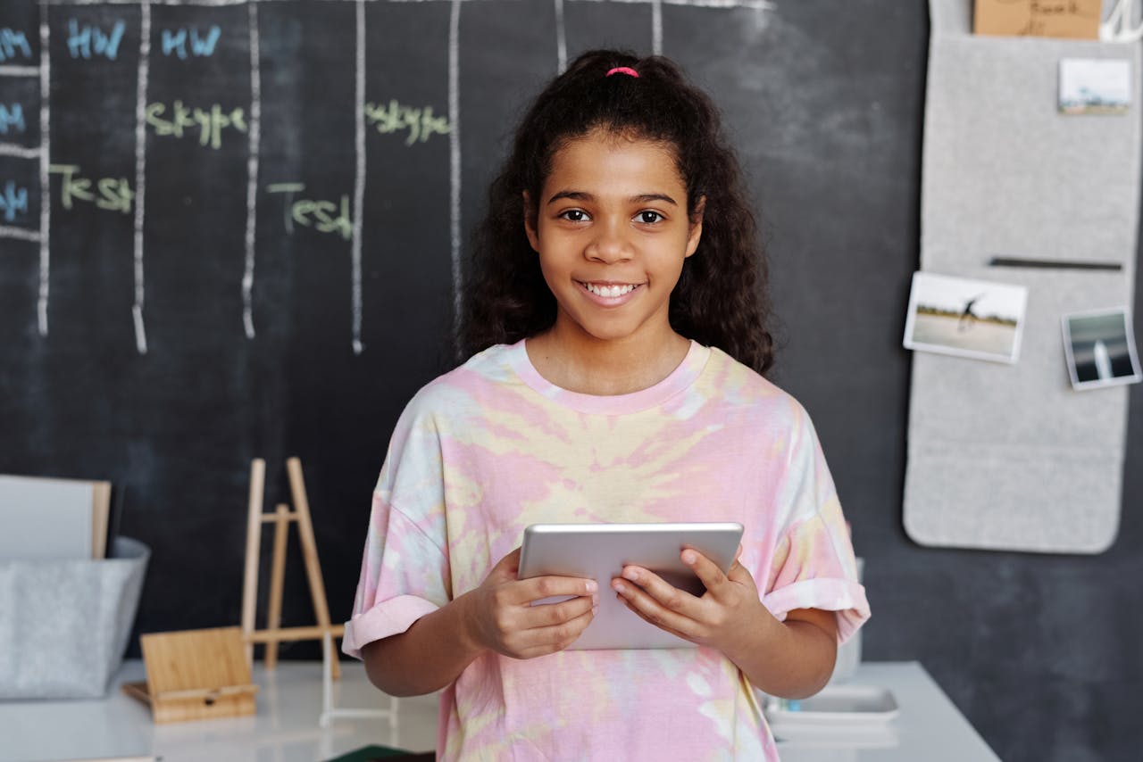 Mastering the First Impression: Your intriguing post title goes here Cheerful girl holding a tablet in a modern classroom with a chalkboard background.